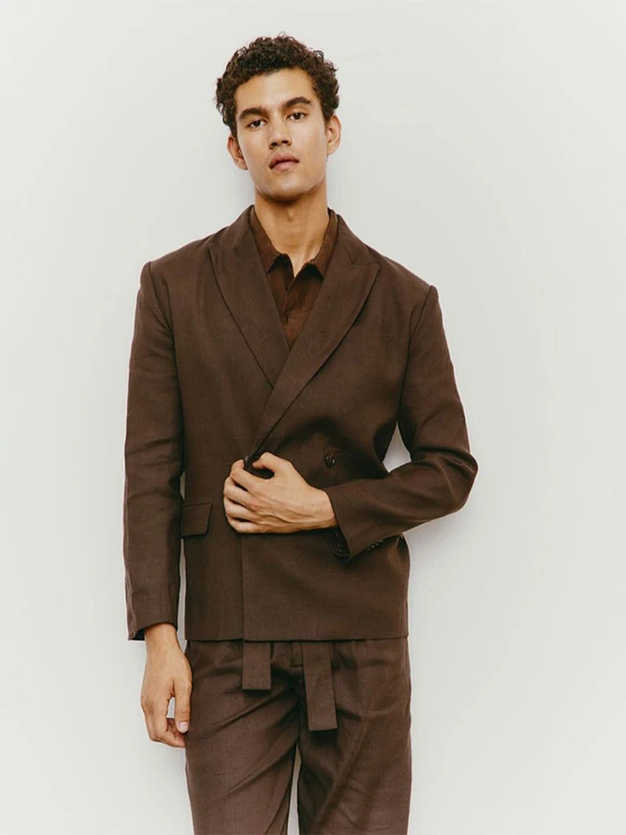Male model wearing a brown double breasted blazer and matching trousers against a white seamless background