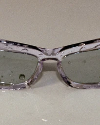 Close-up of translucent purple-tinted sunglasses covered in water droplets on a smooth pale surface for Burberry Summer Stories.