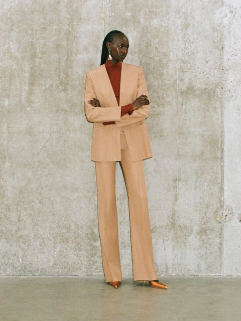 Fashion portrait of an African-descent adult woman wearing a beige pantsuit with a red turtleneck, posing in a photo studio.