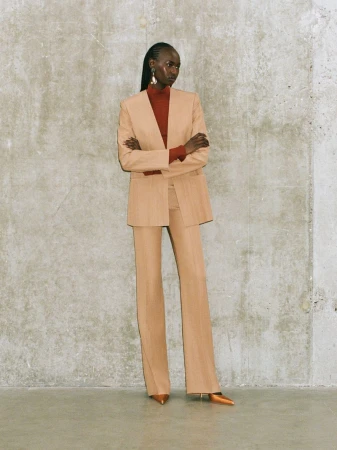 Fashion portrait of an African-descent adult woman wearing a beige pantsuit with a red turtleneck, posing in a photo studio.
