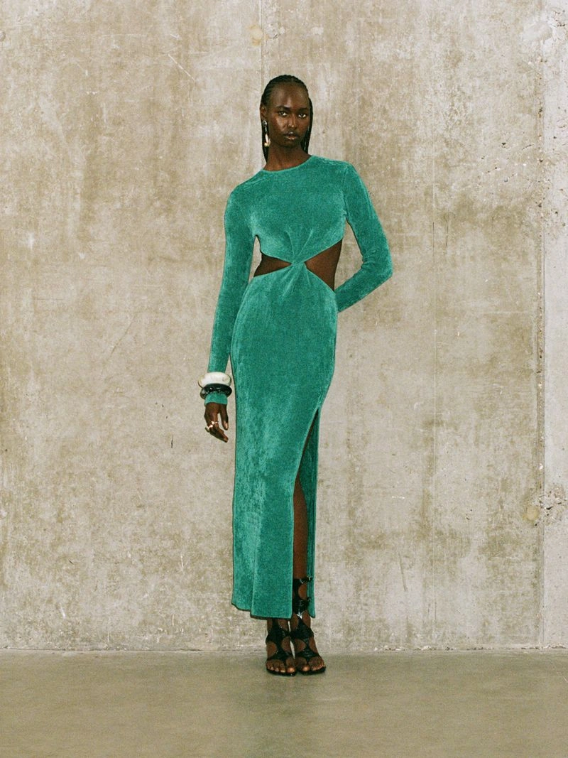 Model in a long green cut-out dress standing against a textured concrete wall for Galvan Pre-Spring 2025.