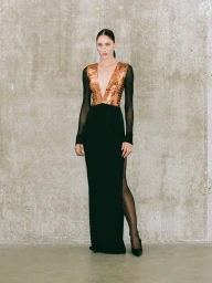 Model standing against a concrete wall wearing a long black evening dress with a metallic bronze plunging V-neck bodice.