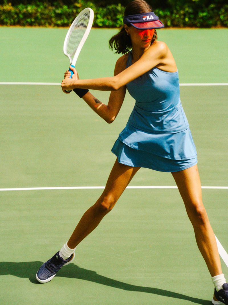 Female tennis player in blue dress hits forehand on green court with white lines, wearing visor, athletic and focused.