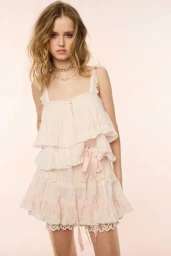 Model in ruffled pale pink top and matching skirt wearing crystal necklaces against a soft neutral background