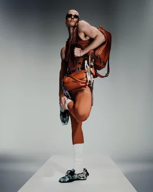 Model Jordan Robson in orange apparel and accessories holding a leather backpack for Acne Studios S/S 25 men's lookbook