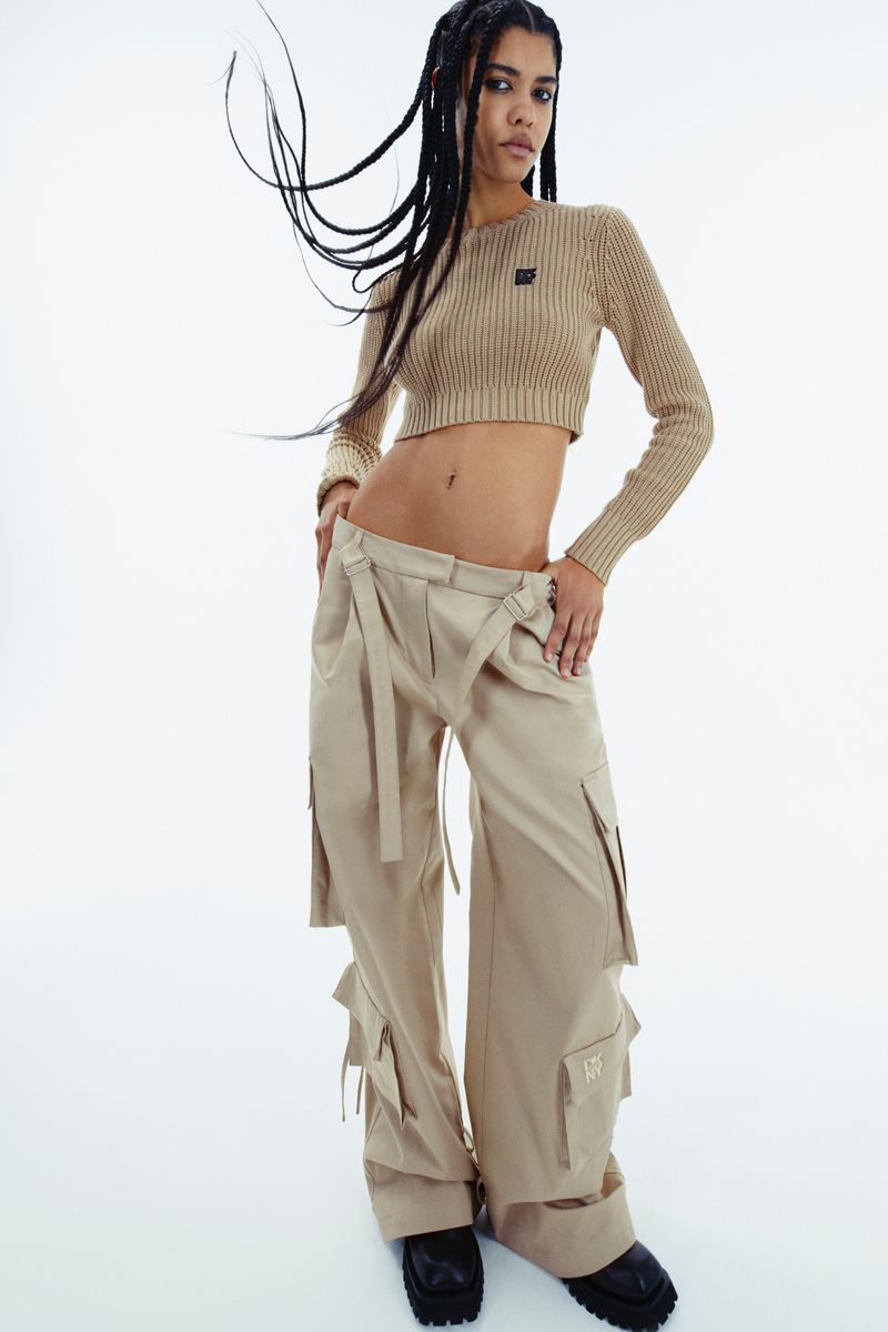 A woman in a crop top and baggy pants poses in a fashion studio, with a neutral color palette and studio lighting on a white backdrop.