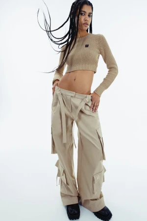 A woman in a crop top and baggy pants poses in a fashion studio, with a neutral color palette and studio lighting on a white backdrop.