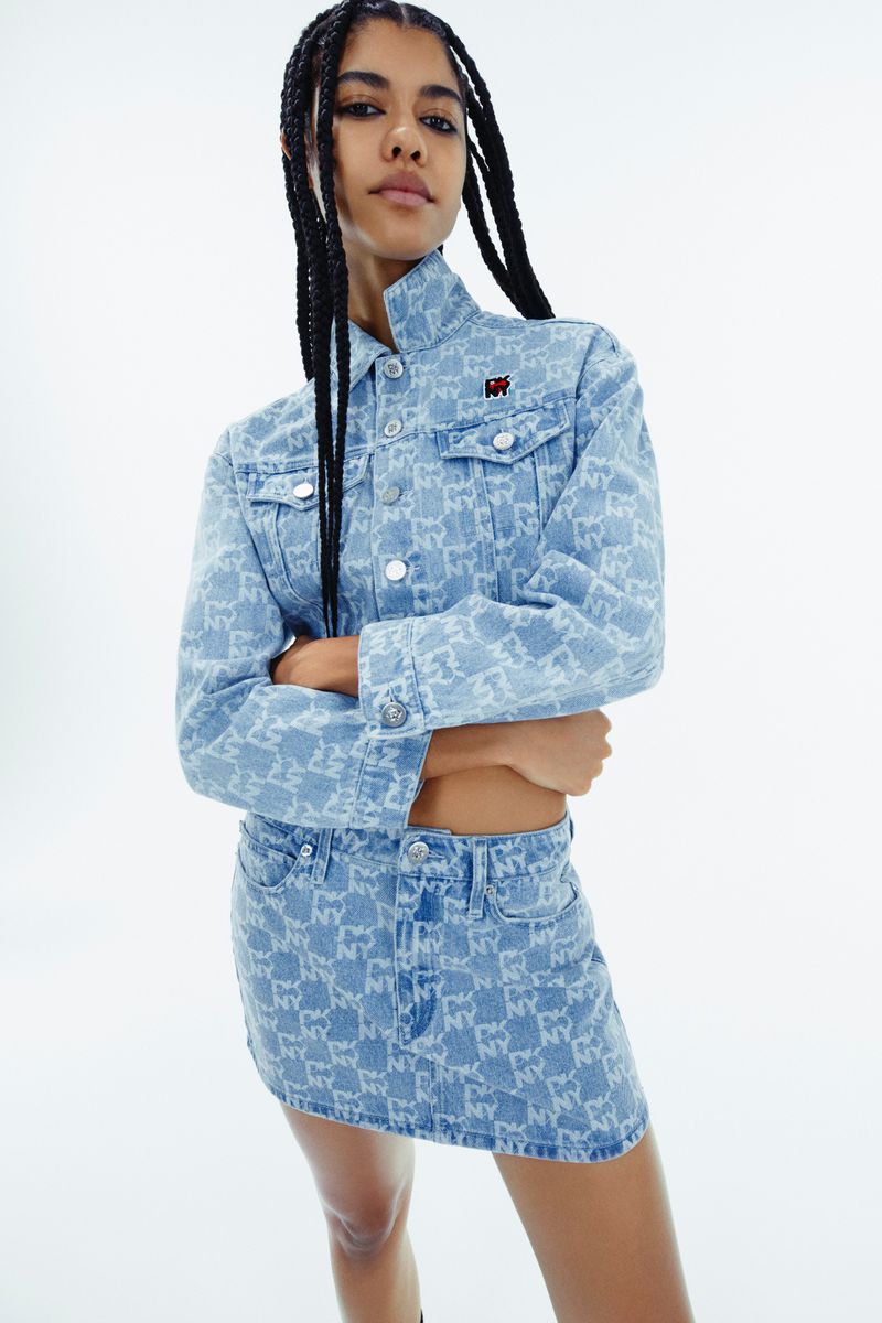 Young woman in a patterned denim jacket and mini skirt poses in a photo studio. The look is completed with long braids.