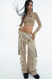 Model with long braided hair wearing a cropped knit top and cargo pants against a white background