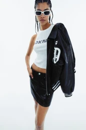 Model wearing white sunglasses and a DKNY logo tank top with a black jacket over her shoulder against a white background.