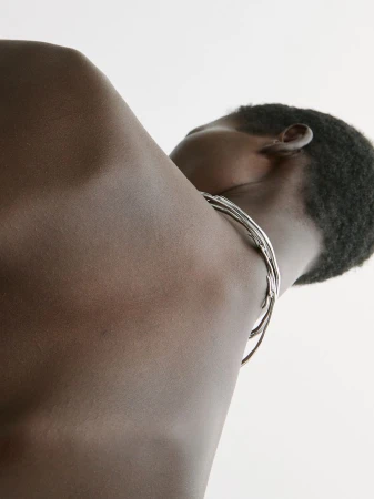 Close-up on an adult with dark skin and short hair, showcasing a silver metal neck choker against a plain white background.