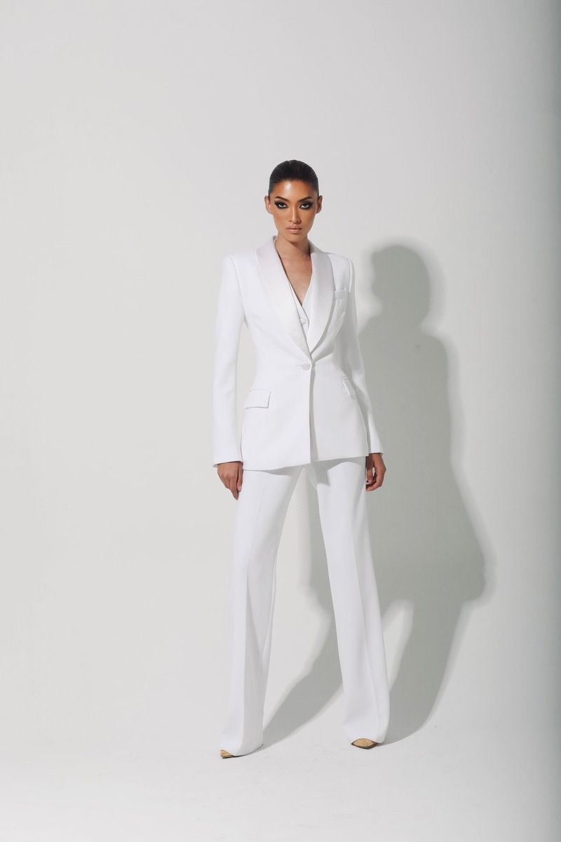 Elegant adult woman in a white suit, standing in a bright photo studio, looking directly at the camera with a neutral expression.