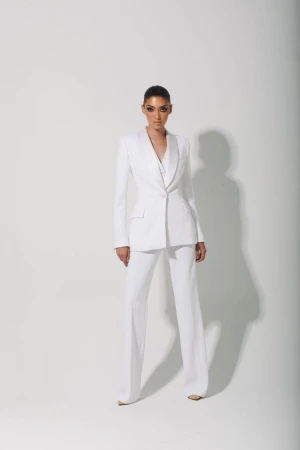 Elegant adult woman in a white suit, standing in a bright photo studio, looking directly at the camera with a neutral expression.