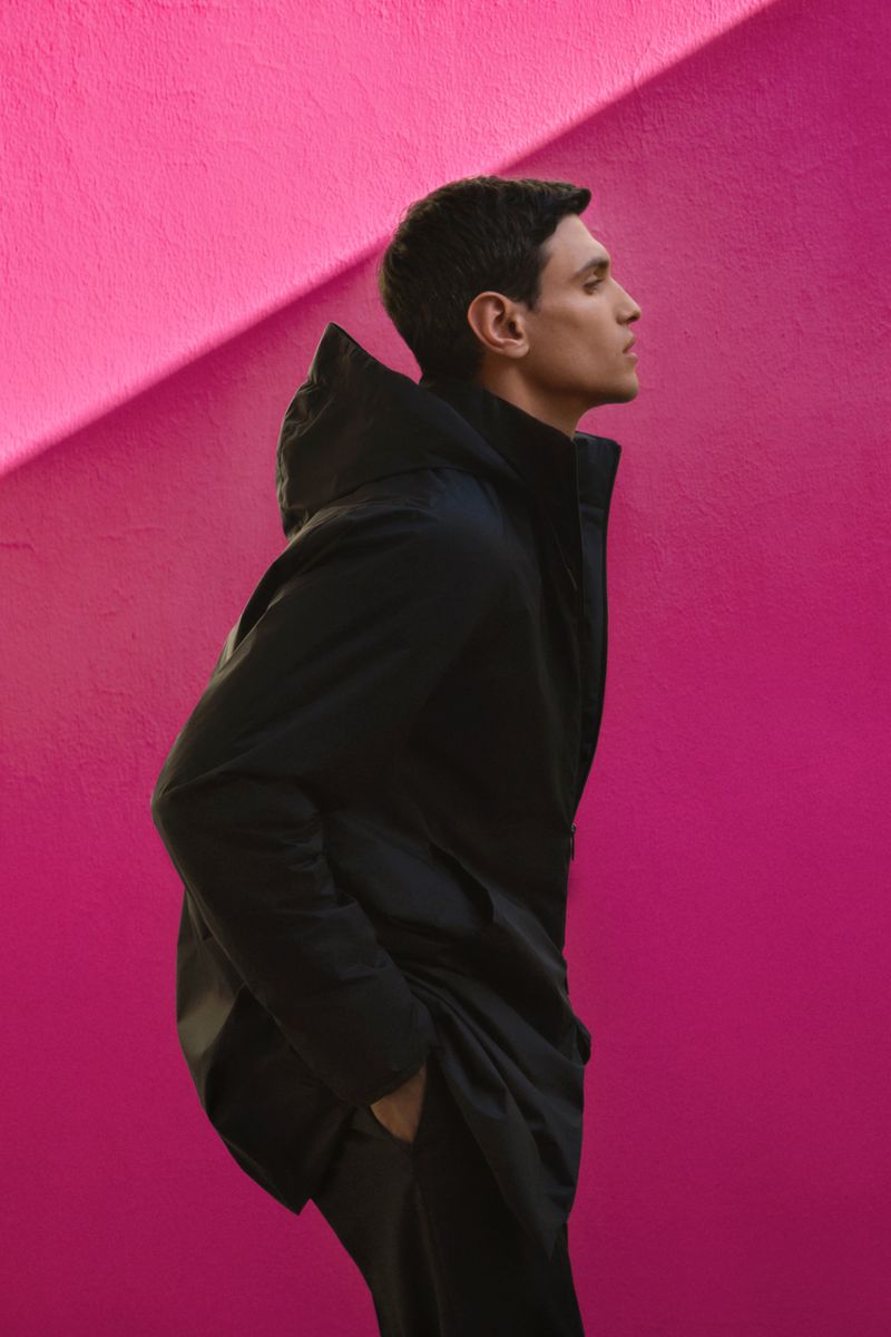 Profile shot of a man in a black jacket against a bright pink wall, emphasizing fashion and urban style with a modern aesthetic.