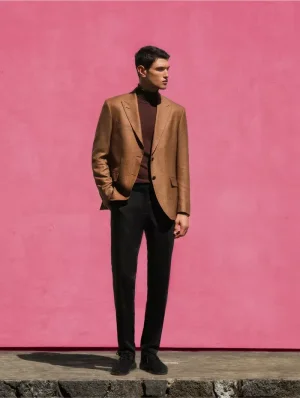 Full-length shot of male model in brown blazer and dark trousers standing against a solid pink wall