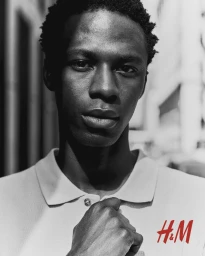 Black man wearing a polo shirt with visible H&M logo in a monochrome portrait shot by James Brodribb.
