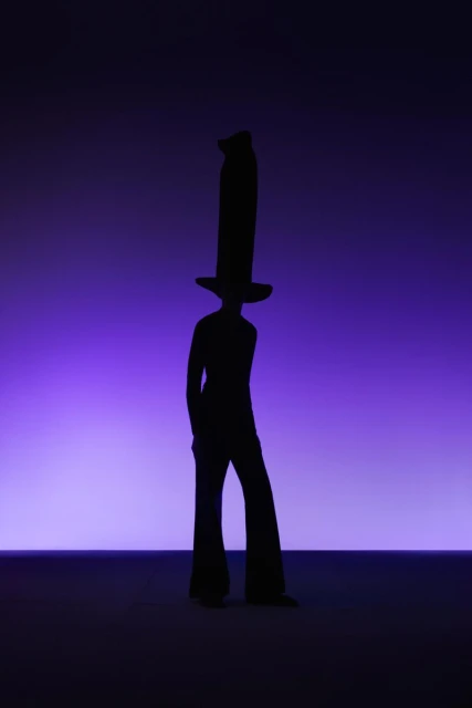 Silhouette of a person with a very tall hat against a gradient purple background, creating a fashion-forward and theatrical image.