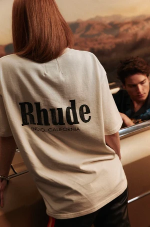 Model with red hair wearing an off-white t-shirt with black branding leaning against a vintage car with another person visible inside.