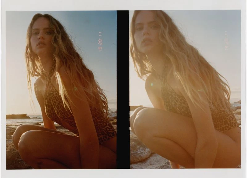 Blonde woman in a leopard print bathing suit crouches on rocks near a beach, bathed in golden light with soft focus and film grain.