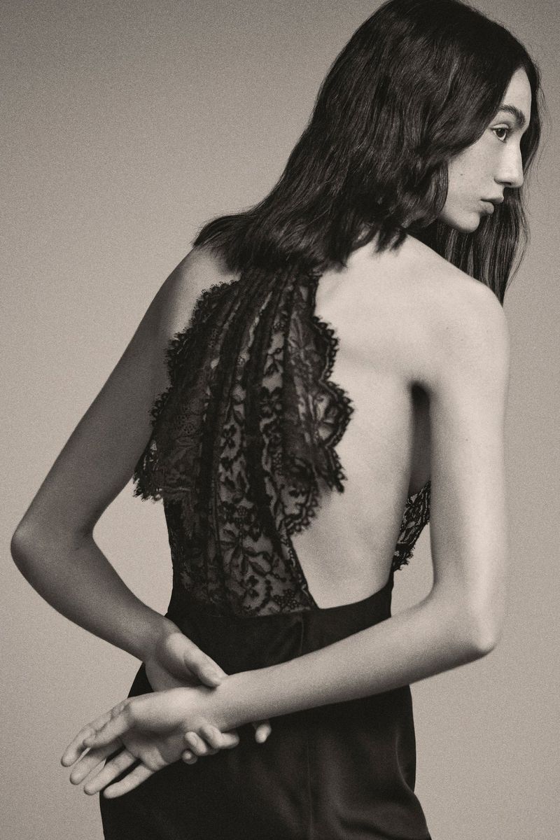 Elegant backless dress with intricate lace detail worn by a woman with long brown hair, captured in a studio fashion shot.