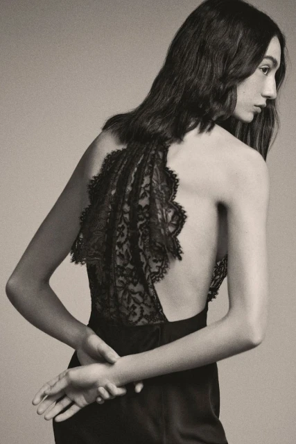 Elegant backless dress with intricate lace detail worn by a woman with long brown hair, captured in a studio fashion shot.