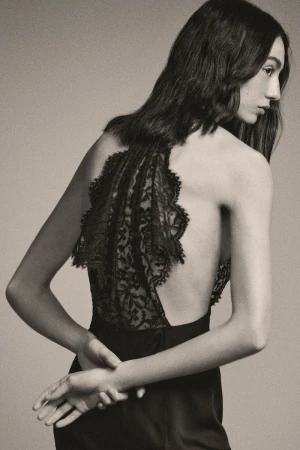 Elegant backless dress with intricate lace detail worn by a woman with long brown hair, captured in a studio fashion shot.