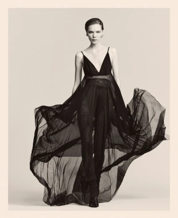 Elegant woman in flowing black dress posing in studio. Fashion shot featuring sheer fabric, black and white tones, and subtle lighting.