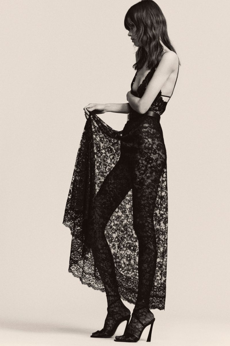 Fashion shot of a woman in a black lace dress with a beige background, showcasing the texture and design details of the garment.