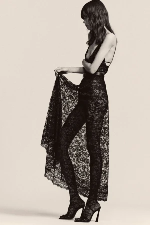 Fashion shot of a woman in a black lace dress with a beige background, showcasing the texture and design details of the garment.
