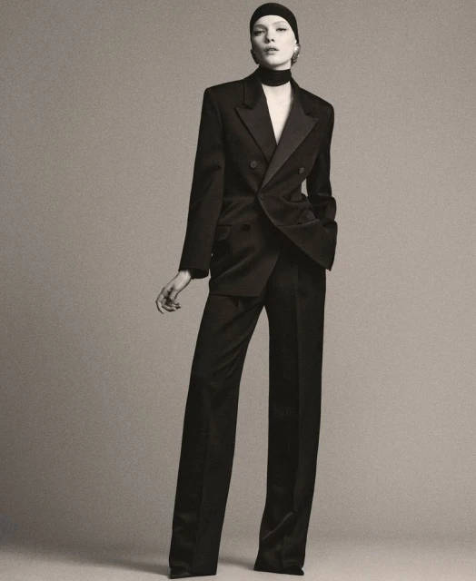 Elegant adult woman in a black suit posing in a studio. The medium shot features a jacket, trousers, and head covering.