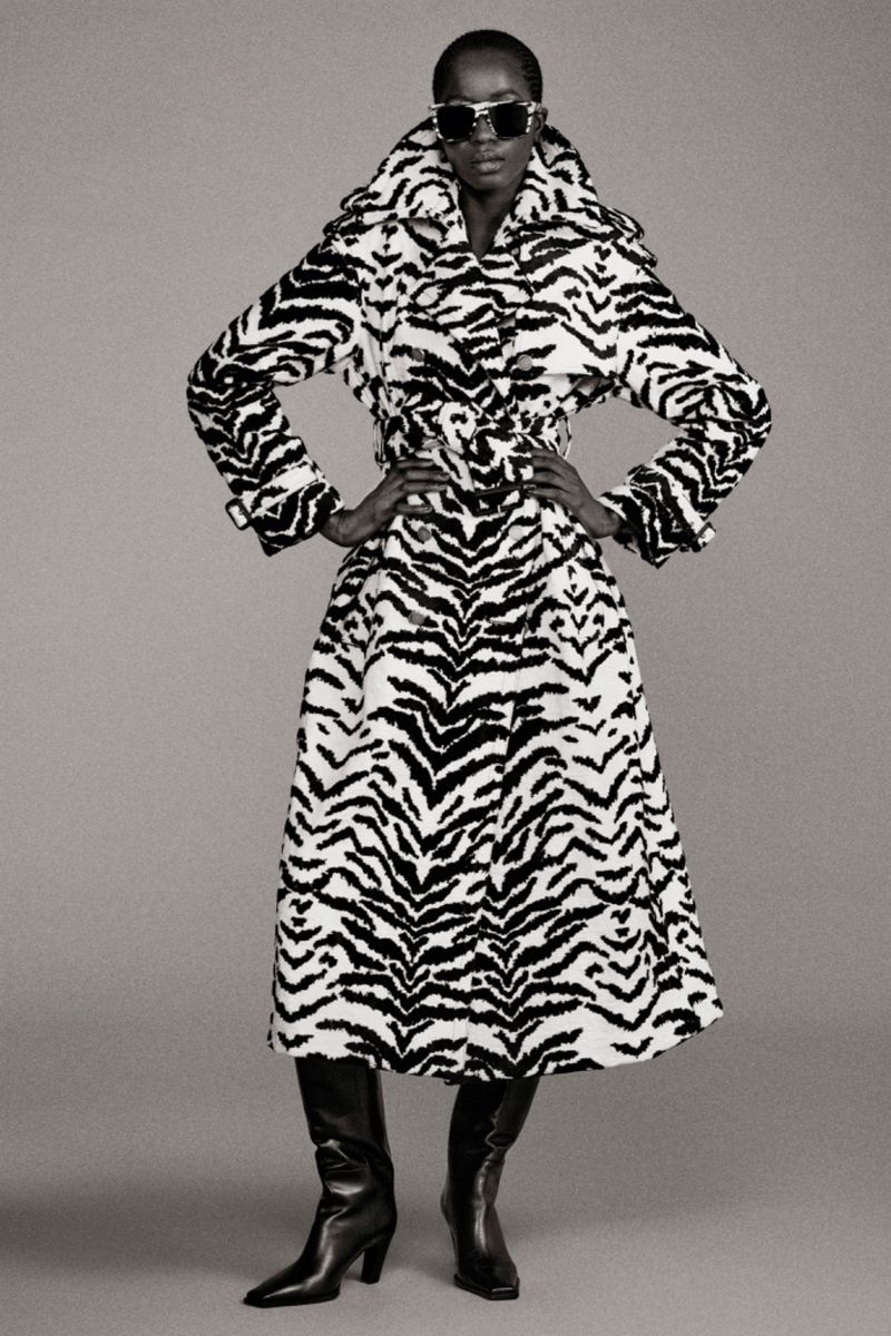 Fashion model wears a zebra-print coat with black leather boots, set against a neutral background in a studio photoshoot.