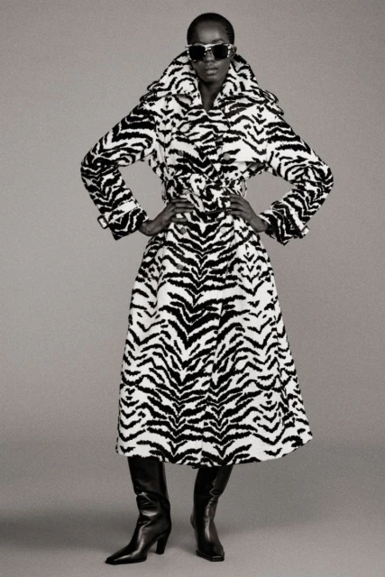 Fashion model wears a zebra-print coat with black leather boots, set against a neutral background in a studio photoshoot.