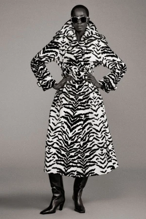 Fashion model wears a zebra-print coat with black leather boots, set against a neutral background in a studio photoshoot.