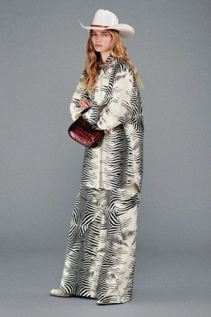 A female fashion model poses in a studio wearing a zebra-patterned suit and cowboy hat, holding a burgundy leather handbag.