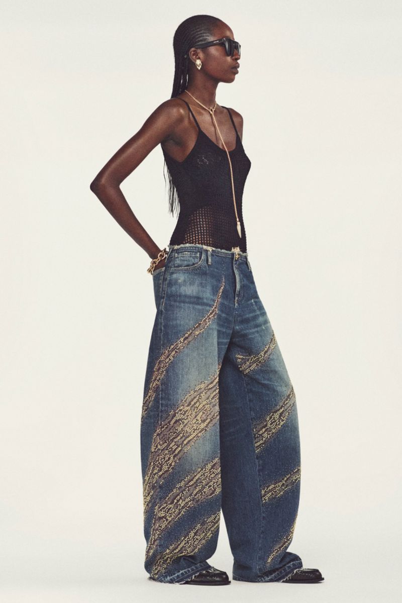 Model in black sunglasses, knit tank top, and wide-leg printed denim jeans against a white studio background.