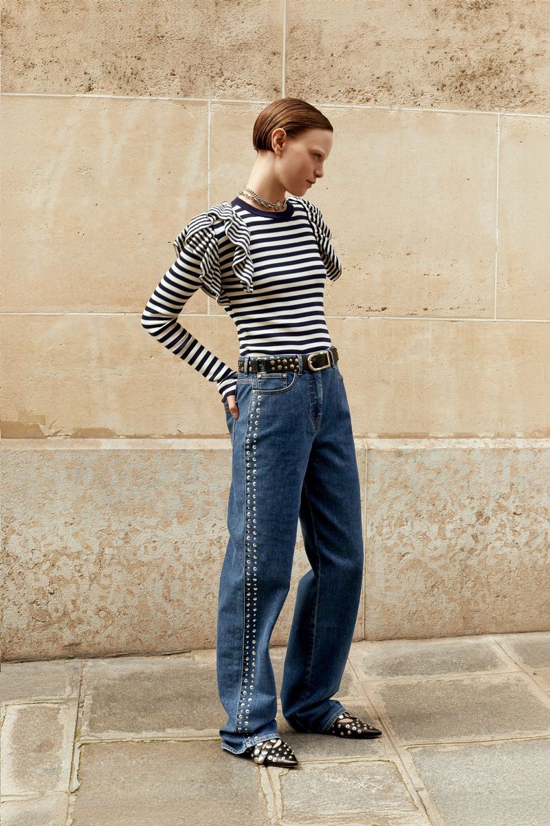A stylish woman poses outdoors in a striped top, wide-leg jeans with studded details, a studded belt, and pointed-toe shoes for a fashion shoot.