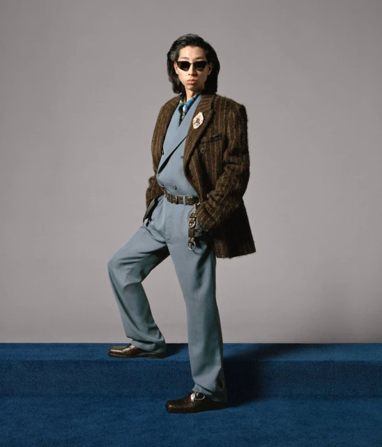 Adult man wearing a double-breasted suit with sunglasses on blue carpet steps in a studio with a neutral grey background.