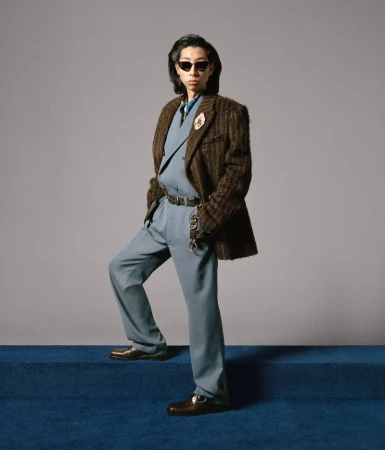 Adult man wearing a double-breasted suit with sunglasses on blue carpet steps in a studio with a neutral grey background.