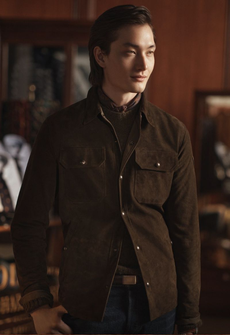 Portrait of a handsome Asian man wearing a brown suede jacket, green shirt, and jeans, posing indoors with a neutral expression.