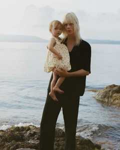 Marjan Jonkman in a black outfit holding a young child in a cream dress on a rocky shoreline for Zara Sea Walk.