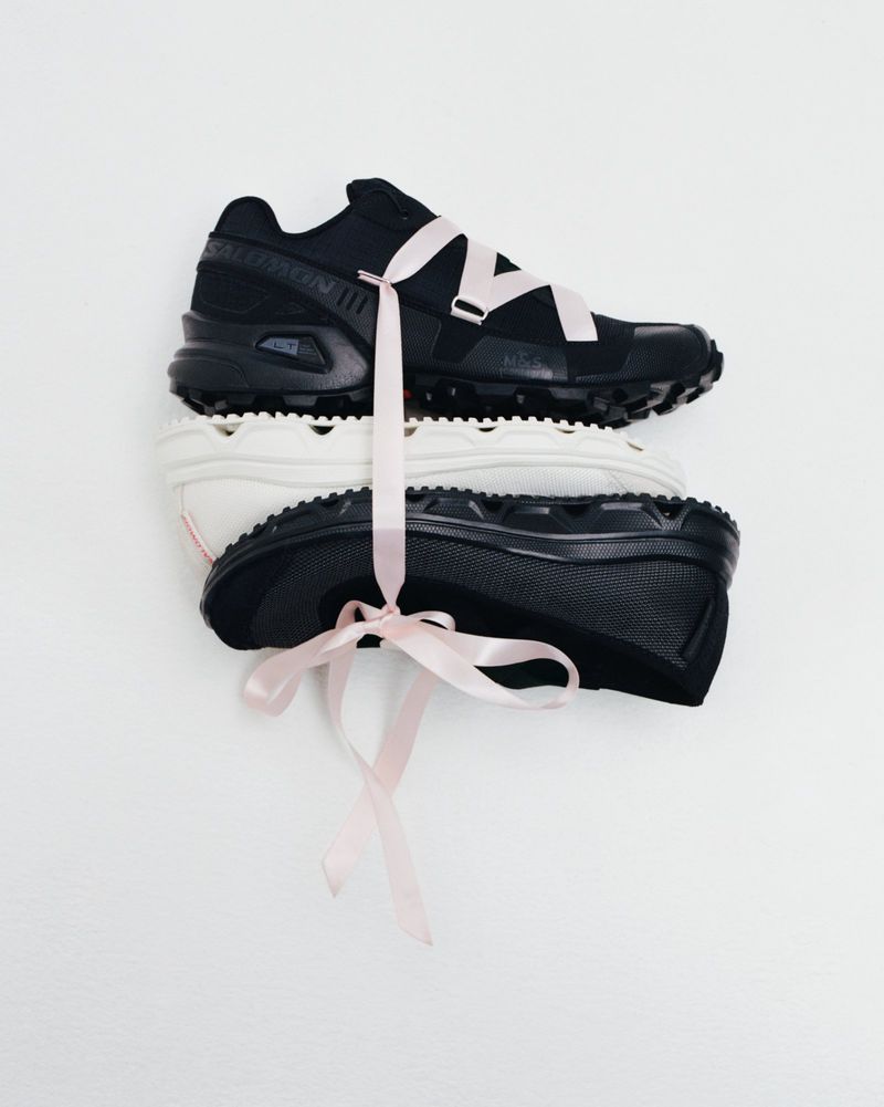 Stack of black and white sneakers tied with a light pink ribbon on a white background, studio product shot, athletic footwear.