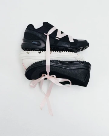 Stack of black and white Salomon sneakers tied together with a light pink satin ribbon against a clean white background.
