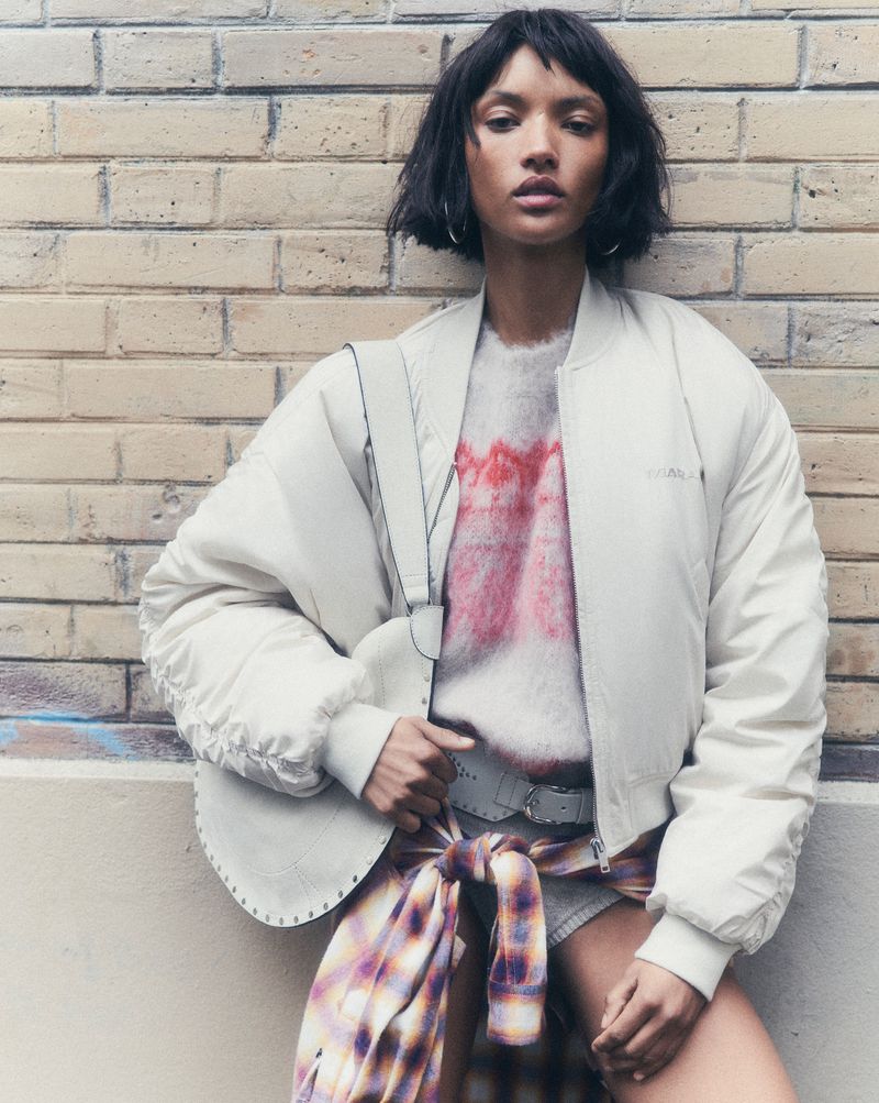 Fashion shot of a woman with short dark hair in an off-white bomber jacket, tie-dye shirt, and plaid shirt tied around her waist.