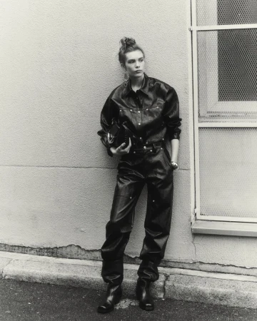 Model Freya Nutter wearing a black leather jumpsuit and boots, leaning against an exterior wall for Isabel Marant.
