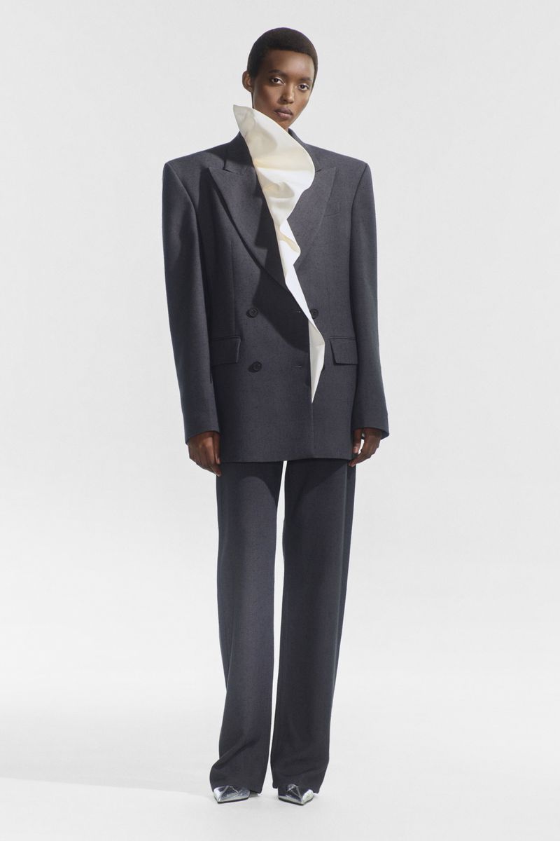 Elegant fashion shot of an African woman in a gray suit with a white ruffled collar, full shot, studio lighting, high fashion, Vogue style.