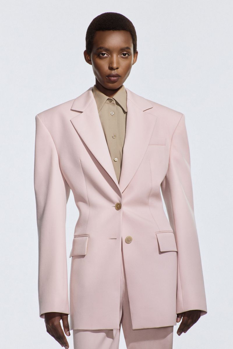 Headshot of an African American woman in a pale pink suit and beige collared shirt against a white background in a fashion setting.