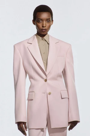 Headshot of an African American woman in a pale pink suit and beige collared shirt against a white background in a fashion setting.