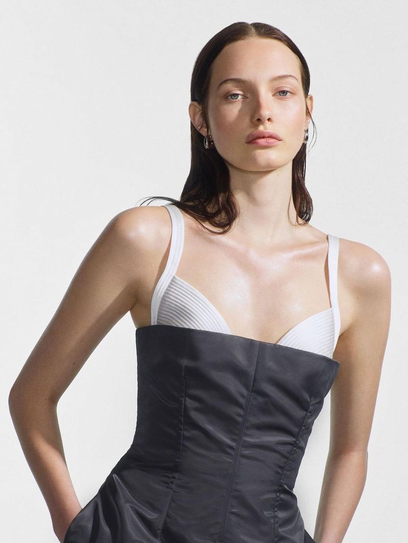 A model poses in a photo studio, wearing a black and white dress, with natural lighting, and a white background for a fashion editorial.