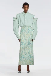 Model wearing a pale mint green cut-out shirt and long patterned column skirt with silver heels against a white studio backdrop.