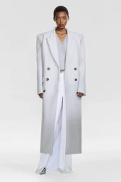 Model Claudia Ishimwe wearing a long double-breasted ombre coat and white wide-leg trousers against a white seamless background.